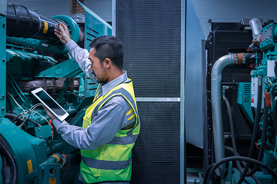 Technician Inspecting Industrial Generator With Tablet