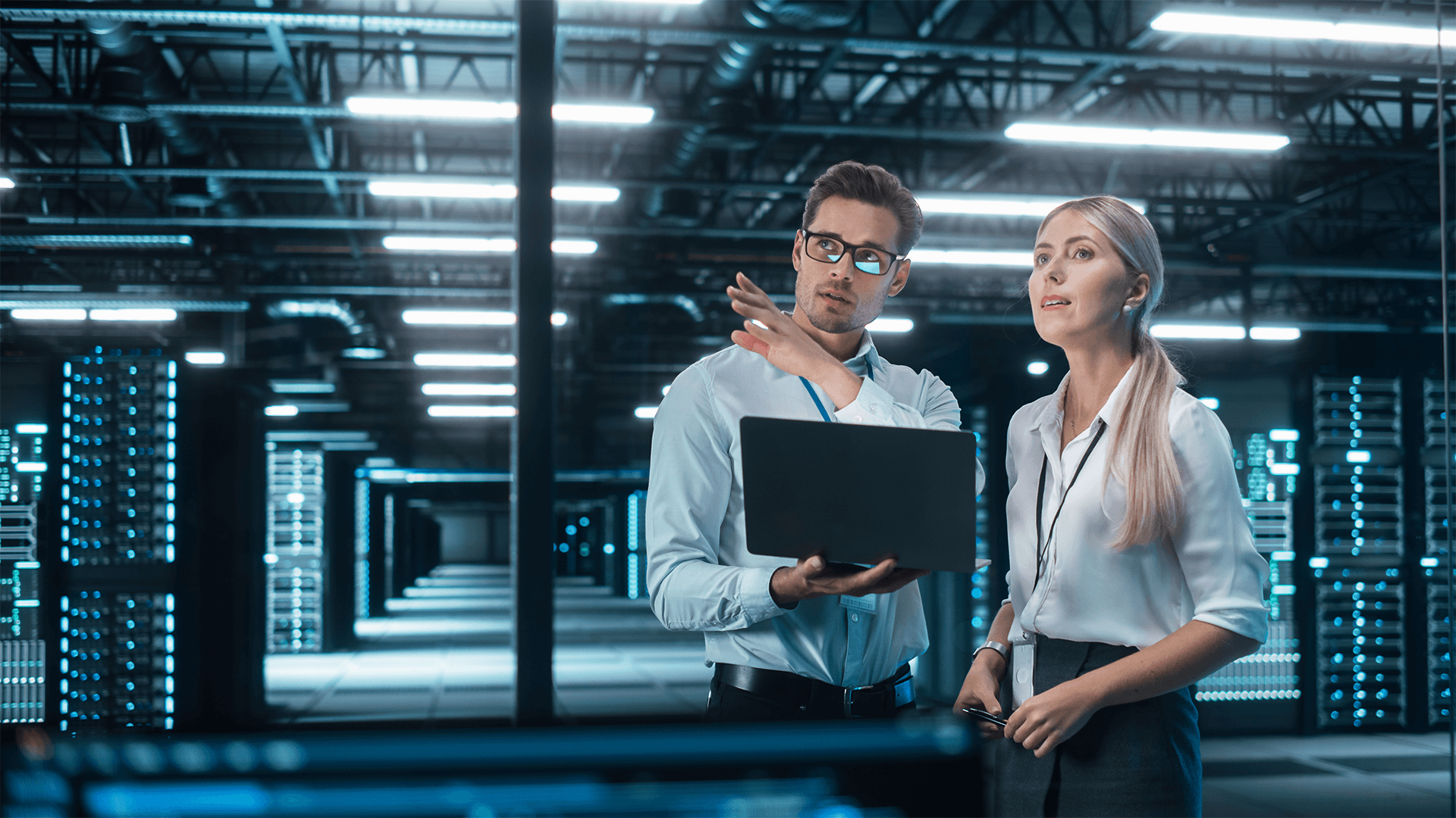 two IT specialists using a laptop and looking out over a data center